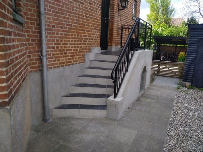 Udendørs trappe ved murstenshus med sort gelænder