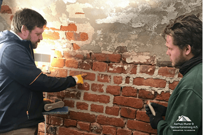 Workers repairing old brick wall indoors