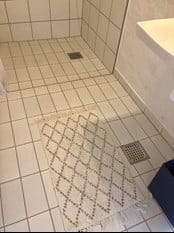 Flisebelagt badeværelse med hvid måtte ved bruseområde